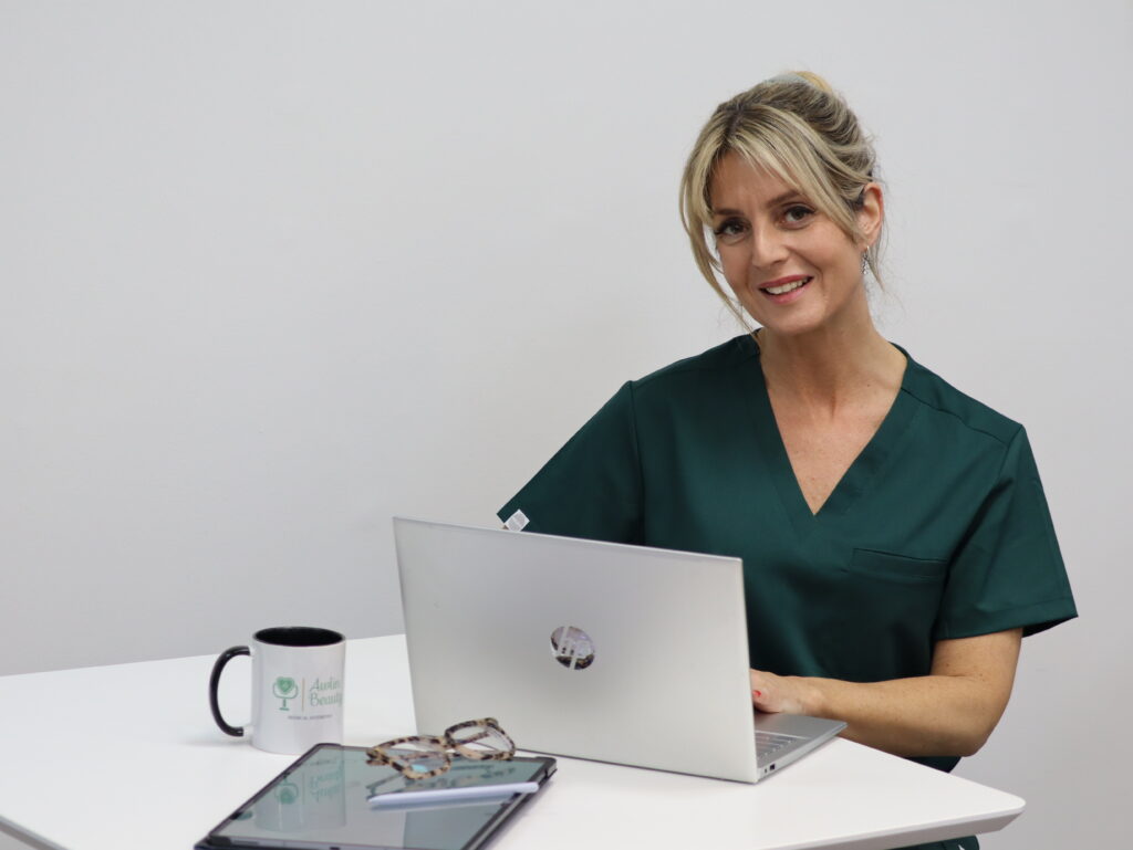 Clare from Awlin Beauty Medical Aesthetics smiling while working on a laptop